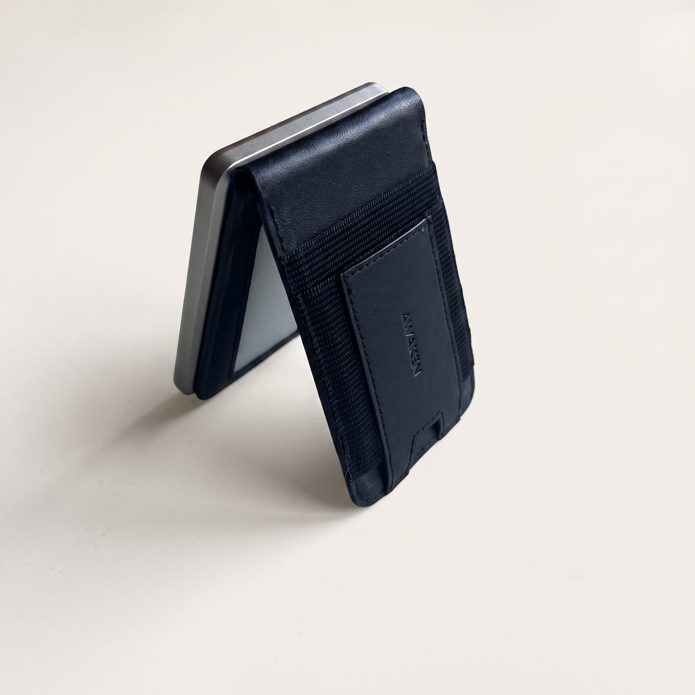AWAKEN PowerWallet i kickstand-läge på varm stenbakgrund — läder, batteri och korthållare